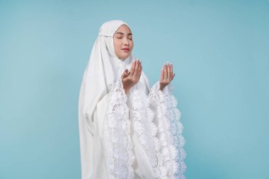 Asyalı Müslüman bir kadının dua elbisesi giymiş, elleri ve mavi arkaplan ile izole edilmiş pozu. Hac kavramı.
