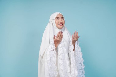 Asyalı Müslüman bir kadının dua elbisesi giymiş, elleri ve mavi arkaplan ile izole edilmiş pozu. Hac kavramı.
