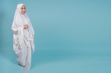 Güzel, Asyalı, genç, Müslüman bir kadın, mavi arka planla soyutlanmış bir şekilde dua elbisesi giyiyor. Hac kavramı.