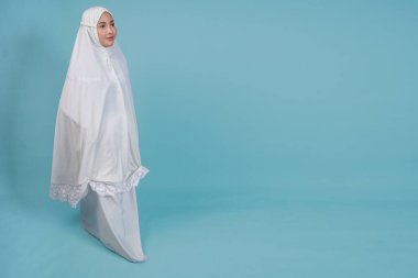 Güzel, Asyalı, genç, Müslüman bir kadın, mavi arka planla soyutlanmış bir şekilde dua elbisesi giyiyor. Hac kavramı.