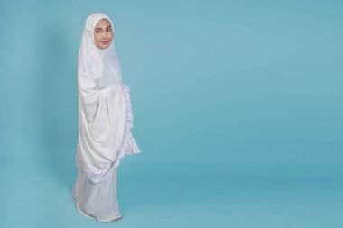 Güzel, Asyalı, genç, Müslüman bir kadın, mavi arka planla soyutlanmış bir şekilde dua elbisesi giyiyor. Hac kavramı.