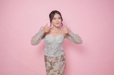 Modern kebaya kıyafetli heyecanlı Endonezyalı kadın pembe arka planla izole edilmiş el hareketleriyle onaylıyor..