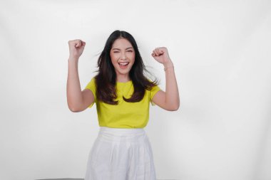 Sarı gömlekli ve beyaz etekli neşeli Asyalı kadın gülümsüyor ve kollarını havaya kaldırıyor. Sevinç ve heyecan kavramı.