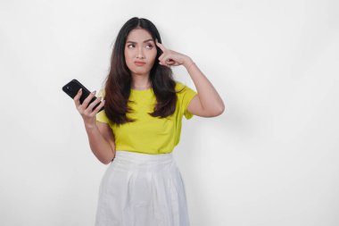 Sarı tişörtlü düşünceli Asyalı kadın elinde bir cep telefonu tutuyor..