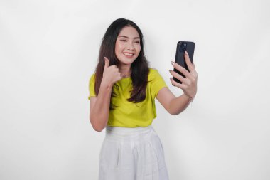 Sarı gömlekli çekici bir kadın cep telefonuyla kendi fotoğrafını çekiyor. Gülümsüyor ve onaylıyor. Bu da mutlu olduğunu ve anın tadını çıkardığını gösteriyor..