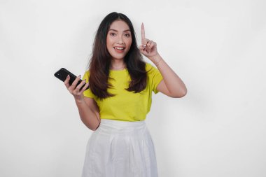 Neşeli genç bir kadın elinde bir cep telefonu tutuyor ve izole edilmiş beyaz arka plan üzerinden fotokopi alanını işaret ediyor..