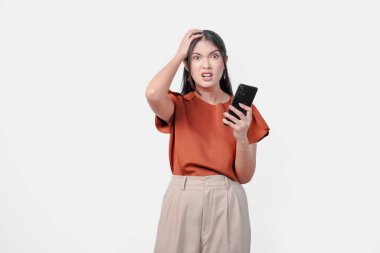 Akıllı telefon tutan Asyalı genç bir kadın üzgün ve izole edilmiş beyaz arka plan yüzünden kızgın görünüyor..