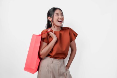 Neşeli genç Asyalı kadın gülümsüyor ve elinde kırmızı bir alışveriş çantası tutuyor. Mutluluk ve heyecan kavramı, çünkü kadın muhtemelen yeni alımlarını kullanmayı dört gözle bekliyor..