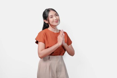 Kahverengi gömlekli barışçıl genç Asyalı kadın beyaz arkaplanda selam veriyor ya da namaste izole edilmiş..