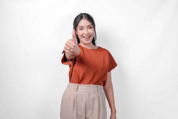 Beautiful young Asian woman in a brown shirt smiling and showing a thumb up gesture, isolated by white background. Concept of happiness and positivity. — Stock Image Beautiful Young Asian Woman Brown Shirt Smiling Showing Thumb Gesture Stock Image
