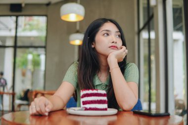 Bir kadın önünde bir dilim pastayla bir masada oturuyor. Üzgün görünüyor ve elini yüzüne doğru tutuyor..