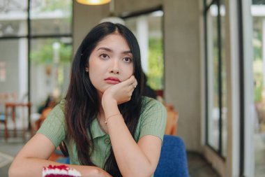 Bir kadın elleri ve çenesini destekleyen bir masada oturuyor, derin düşüncelere dalmış hayal kuruyor..