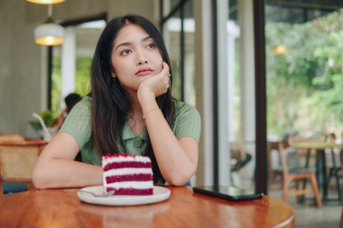 Bir kadın önünde bir dilim pastayla bir masada oturuyor. Üzgün görünüyor ve elini yüzüne doğru tutuyor..