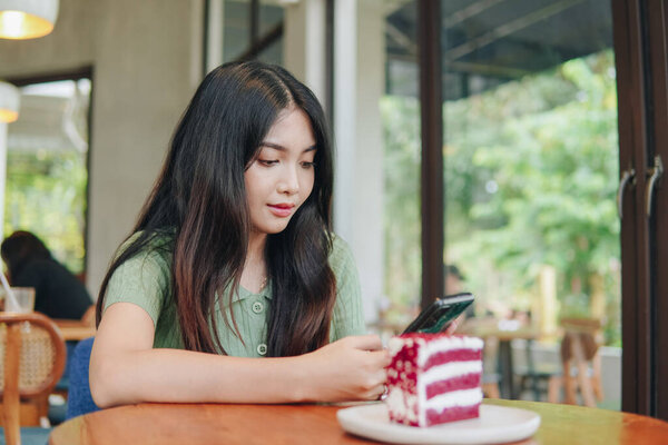 A woman is sitting at a table with a cake in front of her. She is looking at her cell phone. — Stock Image Woman Sitting Table Cake Front Her She Looking Her Cell Royalty Free Stock Images