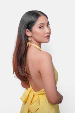 Sarı elbiseli, altın kolyeli ve küpeli, beyaz arkaplanlı güzel Asyalı bir kadının arka portresi..