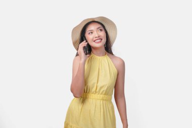 Sarı elbiseli neşeli Asyalı kadın cep telefonuyla konuşuyor. Gülümsüyor ve sohbetten zevk alıyor..
