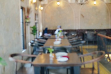 İçinde bir sürü masa ve sandalye olan bir restoranın portresi. Masalar vazo ve çiçeklerle dolu. Sandalyeler ahşap ve siyah. Ortam samimi ve davetkar..