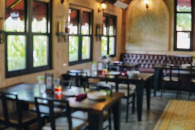 İçinde bir sürü masa ve sandalye olan bir restoranın portresi. Masalar vazo ve çiçeklerle dolu. Sandalyeler ahşap ve siyah. Ortam samimi ve davetkar..