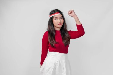 Kırmızı gömlekli ve beyaz pantolonlu çekici genç Asyalı kadın gülümsüyor ve elini havaya kaldırıyor. Endonezya Bağımsızlık Günü kavramı.