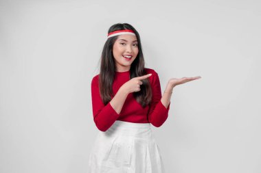 Kırmızı gömlekli ve beyaz pantolonlu neşeli genç bir kadın yanındaki fotokopi odasını işaret ediyor, izole edilmiş beyaz arka plan. Endonezya Bağımsızlık Günü kavramı.