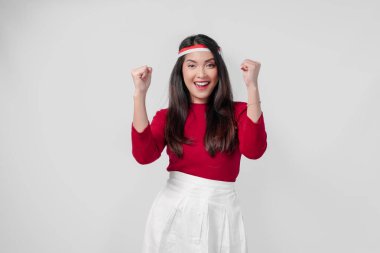 Kırmızı tişörtlü ve beyaz pantolonlu aşırı neşeli genç Asyalı kadın mutlu ve başarılı bir ifadeyle ellerini havaya kaldırıyor. Endonezya Bağımsızlık Günü kavramı.