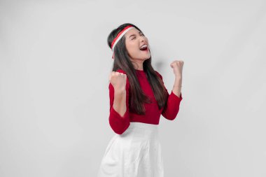 Kırmızı tişörtlü ve beyaz pantolonlu aşırı neşeli genç Asyalı kadın mutlu ve başarılı bir ifadeyle ellerini havaya kaldırıyor. Endonezya Bağımsızlık Günü kavramı.