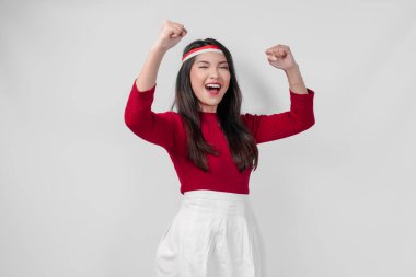 Kırmızı tişörtlü ve beyaz pantolonlu aşırı neşeli genç Asyalı kadın mutlu ve başarılı bir ifadeyle ellerini havaya kaldırıyor. Endonezya Bağımsızlık Günü kavramı.