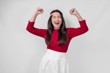 Kırmızı tişörtlü ve beyaz pantolonlu aşırı neşeli genç Asyalı kadın mutlu ve başarılı bir ifadeyle ellerini havaya kaldırıyor. Endonezya Bağımsızlık Günü kavramı.