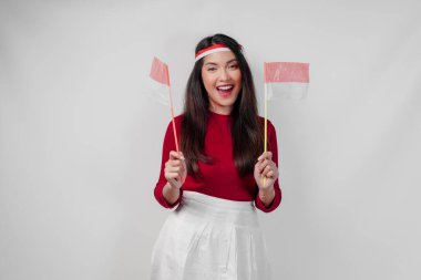 Neşeli genç Asyalı kadın iki bayrak tutuyor ve gülümsüyor, beyaz arka planda soyutlanmış. Endonezya Bağımsızlık Günü kavramı.