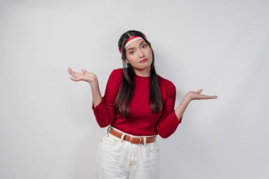 Kırmızı tişörtlü ve beyaz pantolonlu kafası karışmış genç Asyalı kadın elini izole edilmiş beyaz arka planda kaldırıyor. Endonezya Bağımsızlık Günü kavramı.