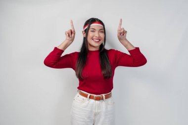 Kırmızı tişörtlü ve beyaz pantolonlu neşeli genç kadın, fotokopi alanını yukarı, izole edilmiş beyaz arka plana işaret ediyor. Endonezya Bağımsızlık Günü kavramı.