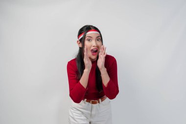 Kırmızı tişörtlü ve beyaz pantolonlu tatlı Asyalı kadın beyaz arka planla izole edilmiş el hareketleriyle fısıldıyor. Endonezya Bağımsızlık Günü kavramı.