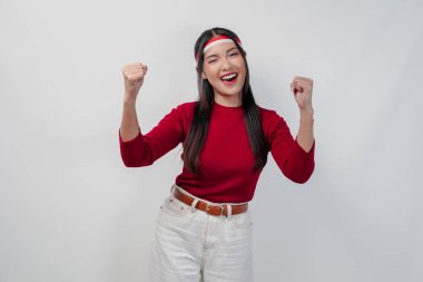 Kırmızı tişörtlü ve beyaz pantolonlu heyecanlı genç Asyalı kadın mutlu ve başarılı bir ifadeyle ellerini havaya kaldırıyor. Endonezya Bağımsızlık Günü kavramı.