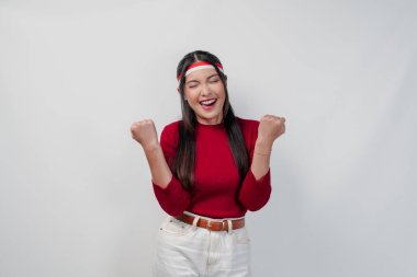 Kırmızı tişörtlü ve beyaz pantolonlu heyecanlı genç Asyalı kadın mutlu ve başarılı bir ifadeyle ellerini havaya kaldırıyor. Endonezya Bağımsızlık Günü kavramı.