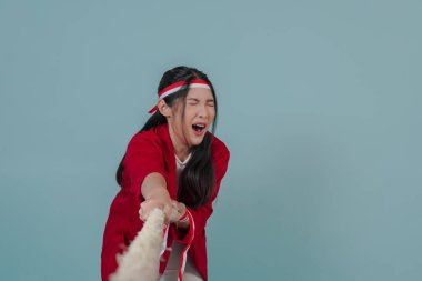 Kırmızı ceketli, ciddi bir Endonezyalı kadın halat çekiyor, bir yarışmada mücadele ediyor. Endonezya Bağımsızlık Günü kavramı.