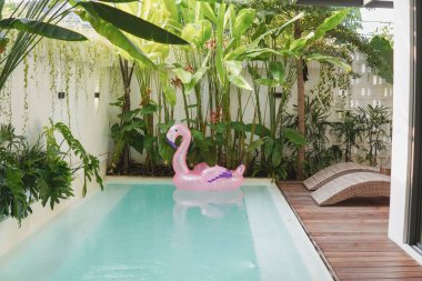 Pembe şişme flamingo havuzda yüzer. Havuz arka bahçede ve güvertede iki tane şezlong var..