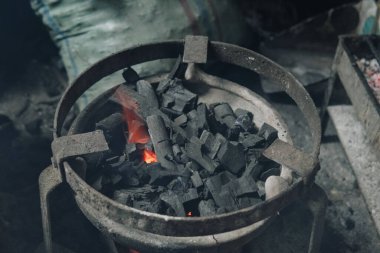 İçinde kömür olan metal bir kase yanıyor. Kase geleneksel bir mutfakta kömür yığınıyla çevrilidir..