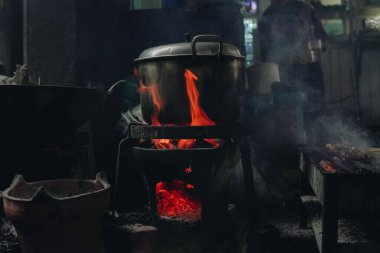 A pot of food is cooking on a stove with a lot of smoke and fire in a traditional kitchen.