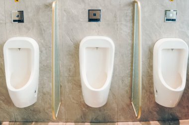 Banyoda aralarında cam bölme olan iki pisuvar. Pisuarlar beyaz ve altın kaplamalı. Banyo temiz ve bakımlı..