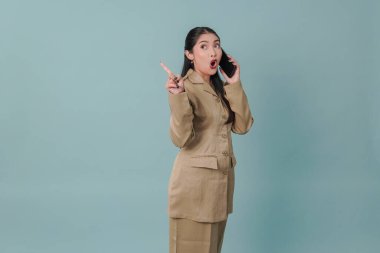 Shocked government worker woman wearing khaki uniform having a call while pointing to the copy space behind her. PNS civil servant concept.