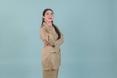 Pretty government worker woman wearing khaki uniform and glasses pointing to the copy space behind her. PNS civil servant concept.