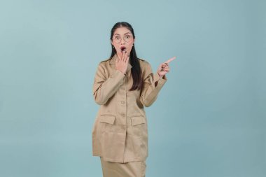 Young government worker woman wearing khaki uniform and glasses pointing to the copy space beside her with shocked expression. PNS civil servant concept.