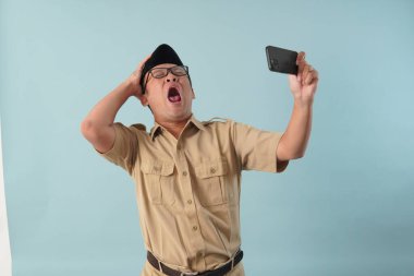 Frustrated Indonesian government worker man wearing khaki uniform while holding smartphone feeling stressed over online loan problem. PNS civil servant concept.