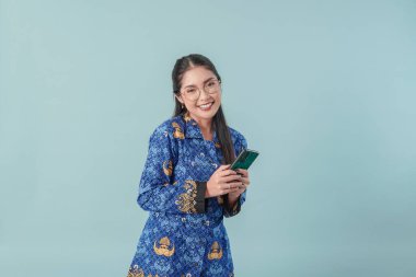 Mavi batik üniformalı ve elinde akıllı telefon tutan gözlüklü heyecanlı bir devlet memuru. PNS devlet memuru kavramı.