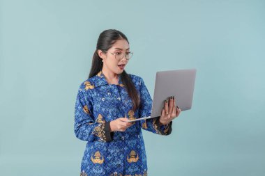 Dizüstü bilgisayarına odaklanmış mavi batik üniformalı ve gözlüklü ciddi bir devlet memuru. PNS devlet memuru kavramı.