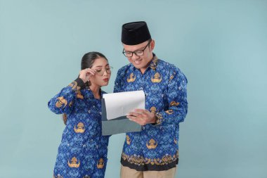 Endonezyalı devlet çalışanları mavi batik üniforma giyip evrak okuyup kontrol ediyorlar ya da ciddi bir ifadeyle rapor veriyorlar. PNS devlet memuru kavramı.