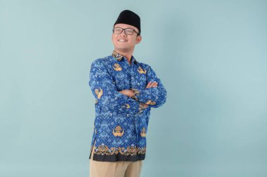 Confident government worker man wearing blue batik uniform smiling with his arms crossed. PNS civil servant concept. clipart