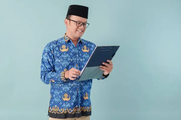 stock image Handsome government worker man wearing blue batik uniform reading and checking document paper. PNS civil servant concept.