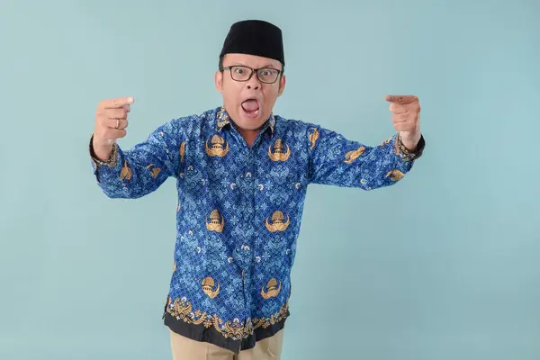 stock image Angry government worker man wearing blue batik uniform raising hands with annoyed expression. PNS civil servant concept.