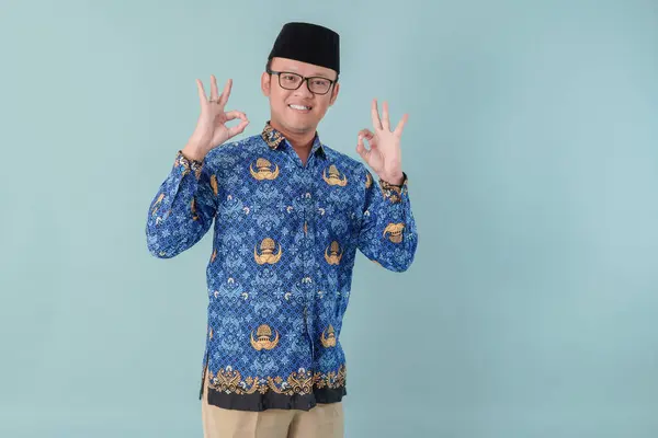 stock image Smiling government worker man wearing blue batik uniform giving OK finger gesture. PNS civil servant concept.